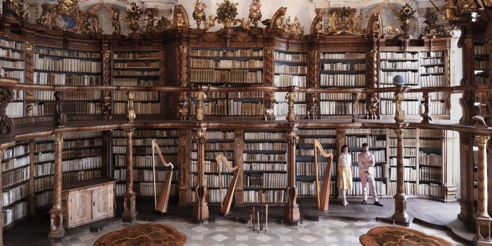 Zwei Menschen in einer alten Bücherei, vorne Harfen und Flöten